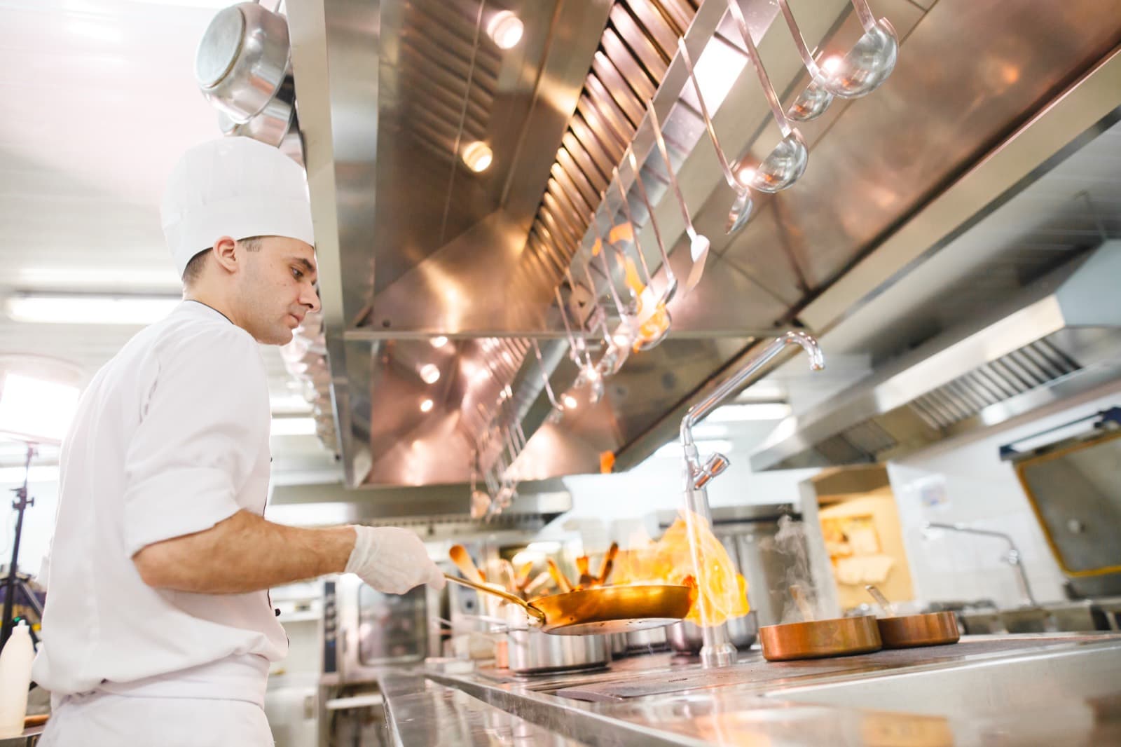 A chef cooking under a stainless steel commercial kitchen exhaust hood.