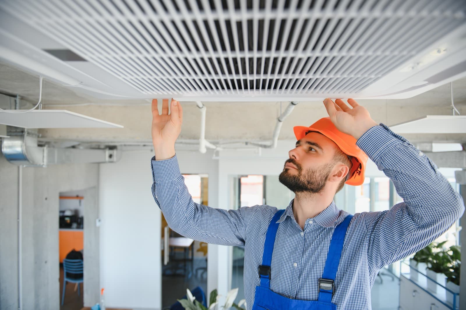 A technician in a hard hat inspecting a ceiling HVAC vent during a service call.