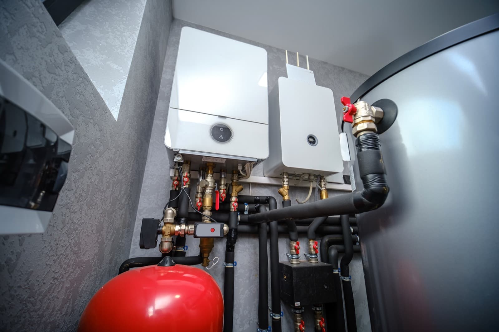 Commercial water heaters, a storage tank, and piping in a mechanical room.