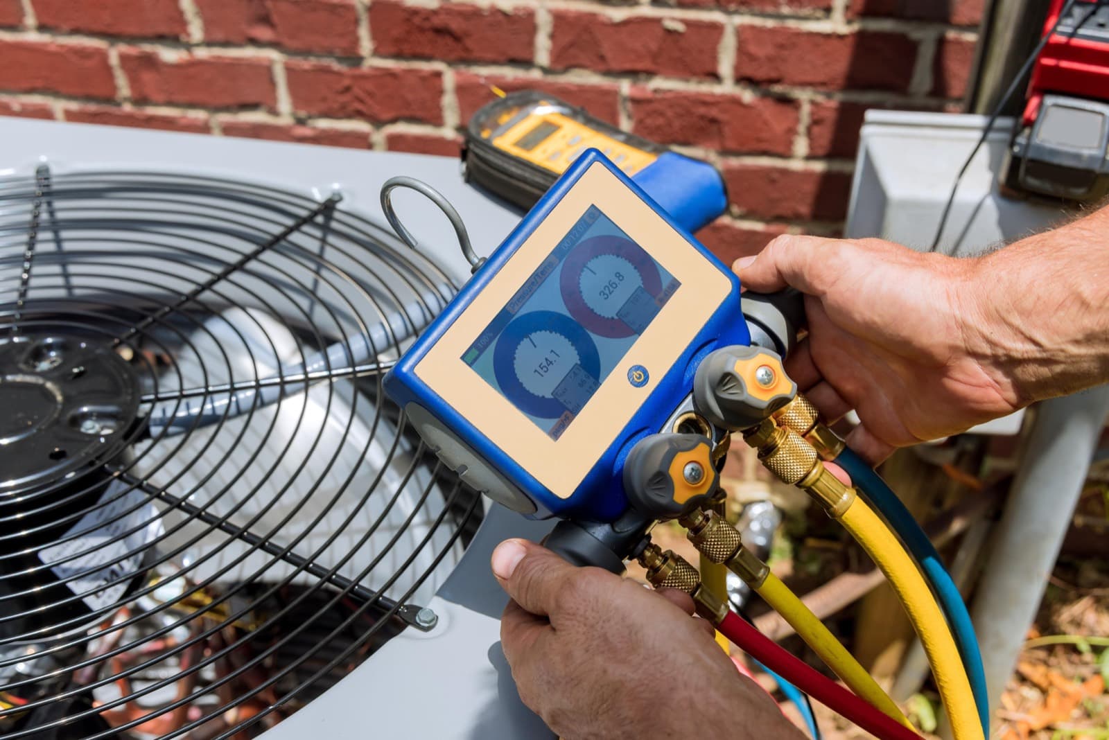 A technician reading a digital manifold gauge on an outdoor HVAC unit.