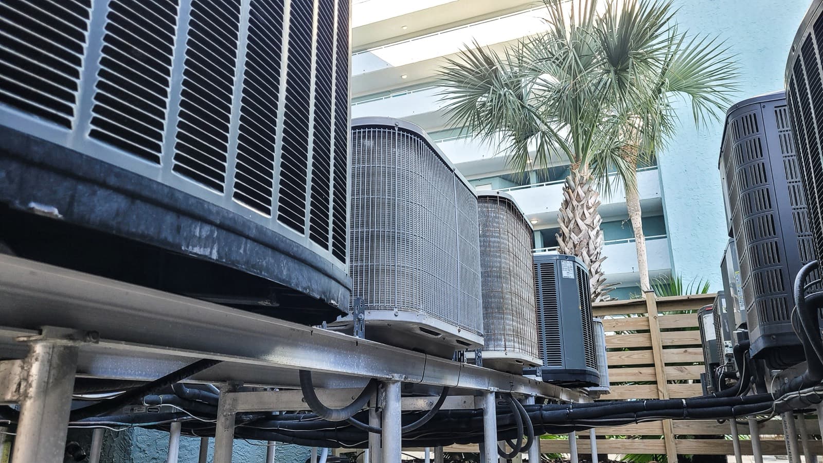 A row of outdoor commercial HVAC condenser units beside a building in a warm climate.